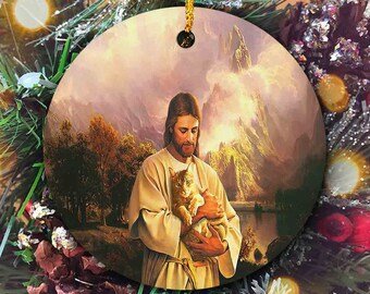 Può includere: Un ornamento rotondo in ceramica con un dipinto di Gesù che tiene un gatto tra le braccia. Lo sfondo è un paesaggio con montagne e un lago. L'ornamento è perfetto per gli amanti dei gatti e i cristiani.