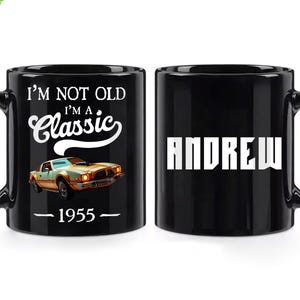 Może przedstawiać: Czarny ceramiczny kubek z napisem "I'M NOT OLD I'M A Classic" i grafiką zabytkowego samochodu. Rok "1955" znajduje się pod grafiką. Druga strona kubka ma imię "ANDREW" białymi literami. Zielone logo "Customize" znajduje się w lewym górnym rogu.
