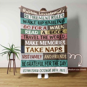 May include: A personalized retirement rules blanket with a woodgrain background. The blanket features the name "Robbie Lovestrand's" and the text "Retirement Rules" in a colorful font. The text "Established October 30th, 2021" is at the bottom of the blanket.