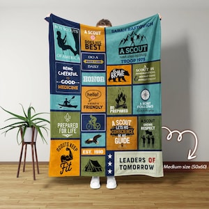 May include: A blue and green fleece blanket with a Boy Scouts theme. It features a variety of scout-related images and text, including "A Scout Does His Best", "Be Prepared", and "Leaders of Tomorrow".