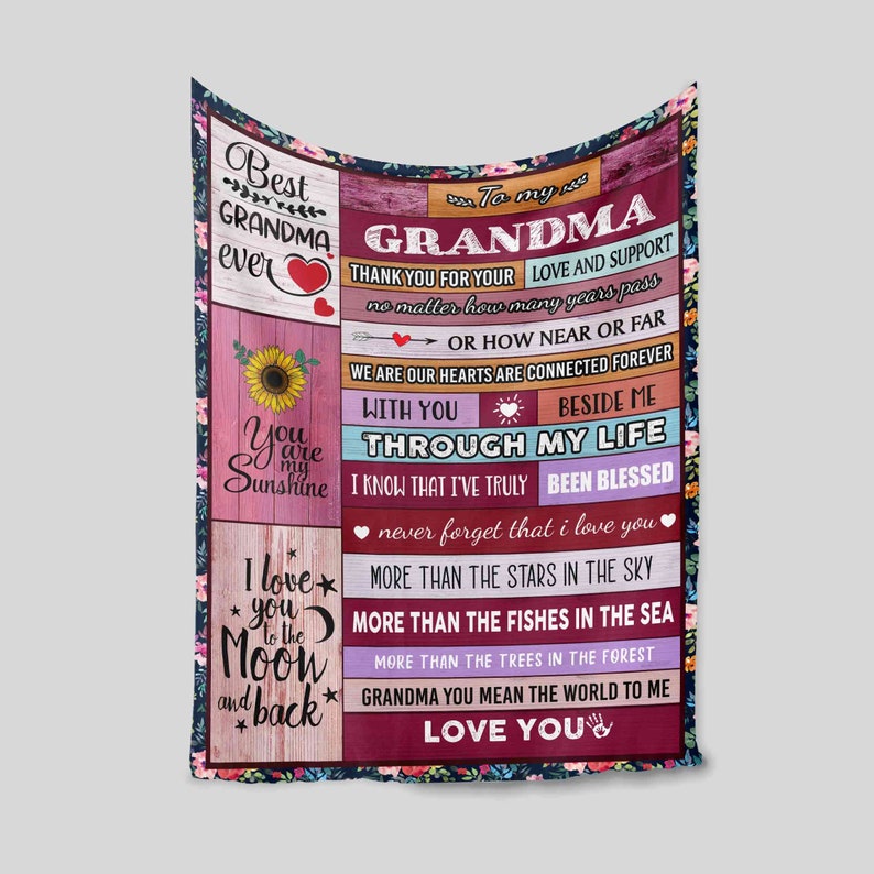May include: A pink and red fleece blanket with a floral design and the text "To my Grandma" and "Best Grandma Ever". The blanket also features a sunflower, a heart, and the text "I love you to the moon and back".
