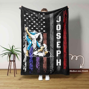 Könnte beinhalten: Eine schwarze Fleece-Decke mit dem personalisierten Namen "JOSEPH" in weiß gedruckt. Die Decke zeigt ein verblasstes amerikanisches Flaggen-Design mit einer Grafik von zwei Personen in einem Jiu-Jitsu-Match. Die Decke ist 127 cm x 152 cm groß.