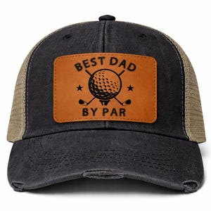 Może przedstawiać: Czarna i beżowa czapka typu trucker z postarzanym wykończeniem. Z przodu brązowa skórzana naszywka z napisem "BEST DAD BY PAR" oraz grafiką piłki i kija golfowego. Czapka ma siatkowy tył i zakrzywiony daszek.