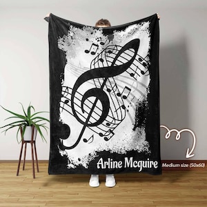Può includere: Coperta in bianco e nero con un grande disegno di chiave di violino e note musicali. La coperta ha uno sfondo invecchiato e il nome "Arline McGuire". La coperta è di medie dimensioni, 127x152 cm.