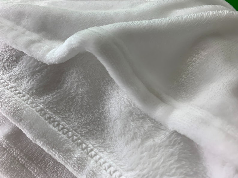 May include: Close-up of a white plush blanket with a stitched edge. The blanket is soft and fluffy, and the stitching is visible.