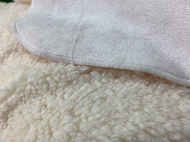 May include: Close-up of a white plush blanket with a soft, fluffy texture. The blanket has a white fleece lining on one side and a white sherpa lining on the other side.