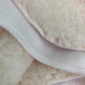 May include: Close-up of a white, fluffy fabric with a stitched seam. The fabric is folded over itself, revealing a soft, plush texture.
