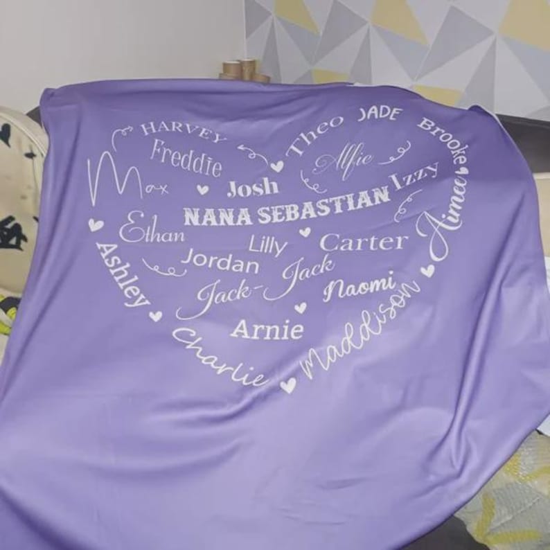 K&ouml;nnte beinhalten: Eine lavendelfarbene Decke mit einem herzf&ouml;rmigen Design, das mit Namen in wei&szlig;er Schrift gef&uuml;llt ist. Zu den Namen geh&ouml;ren Harvey, Freddie, Max, Josh, Nana Sebastian, Lilly, Jordan, Jack, Arnie, Charlie, Ashley, Theo, Jade, Alfie, Izzy, Carter, Naomi, Maddison und Aimee.