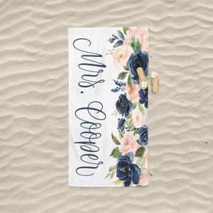 May include: White beach towel with a navy blue and pink floral design. The text "Mrs. Cooper" is written in navy blue cursive on the left side of the towel.
