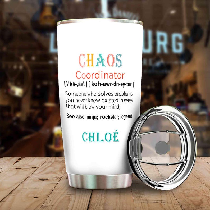 May include: White tumbler with a silver lid, featuring the text "CHAOS Coordinator" in colorful letters. The tumbler includes a definition and the name "CHLO&Eacute;" in teal. The design is on a wooden surface.