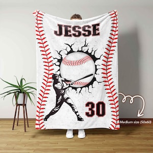May include: White baseball-themed blanket with red stitching along the edges. Features a baseball graphic bursting through a cracked wall, a batter silhouette, the name "Jesse" in bold letters, and the number "30".