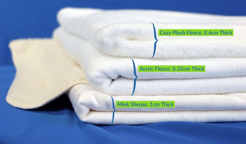 May include: Three white fleece blankets stacked on top of each other. The top blanket is labeled "Cozy Plush Fleece, 0.6cm Thick", the middle blanket is labeled "Arctic Fleece, 0.35cm Thick", and the bottom blanket is labeled "Mink Sherpa, 1cm Thick".