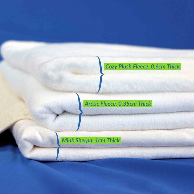 May include: A stack of three white fleece blankets, labeled with their thickness and type: Cozy Plush Fleece, 0.6cm thick; Arctic Fleece, 0.35cm thick; Mink Sherpa, 1cm thick.