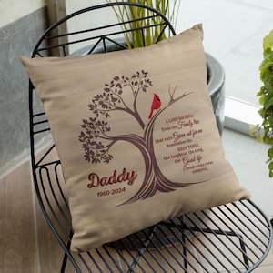 Puede incluir: Un cojín cuadrado beige con un diseño de árbol y un cardenal rojo. El árbol tiene la palabra "Daddy" y los años "1960-2024" impresos. El texto en el cojín dice "Una rama ha caído del árbol genealógico..."