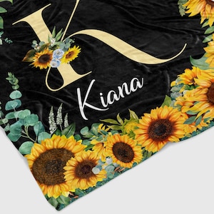 May include: Black fleece blanket with a large yellow letter K and the name Kiana in white text. The blanket is decorated with sunflowers and eucalyptus leaves.
