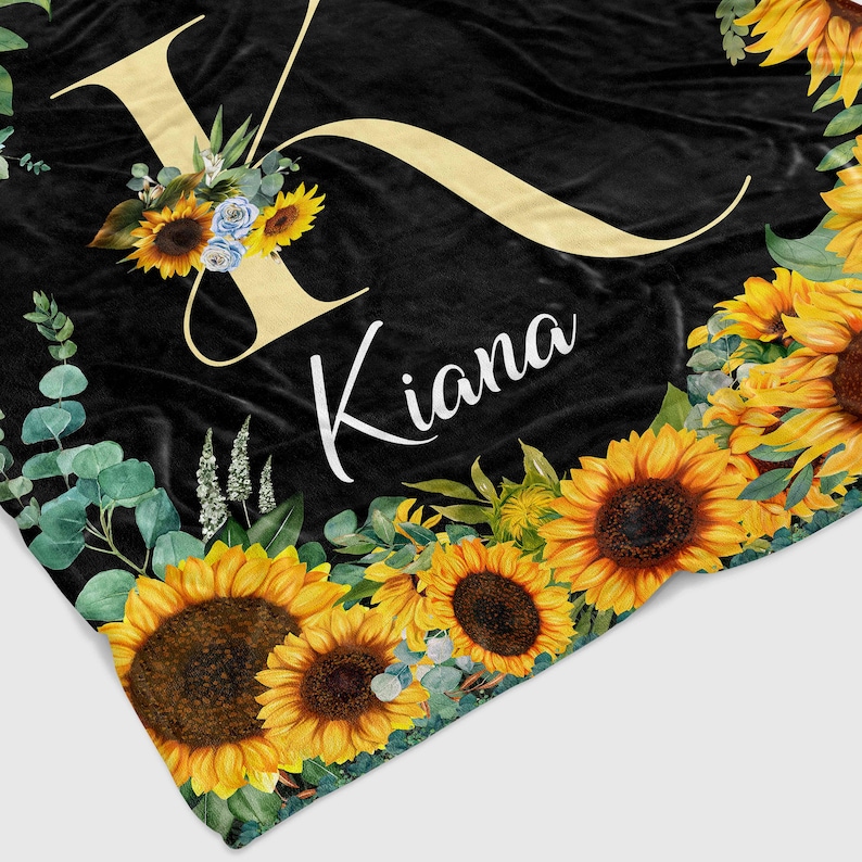 May include: Black fleece blanket with a large yellow letter K and the name Kiana in white text. The blanket is decorated with sunflowers and eucalyptus leaves.