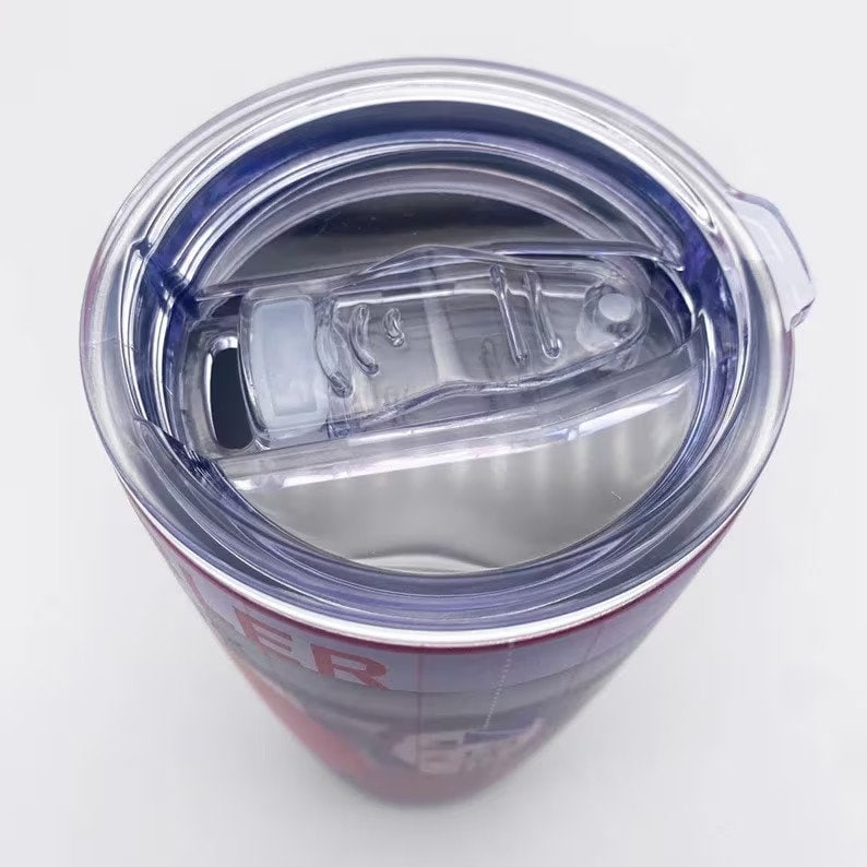 May include: A stainless steel tumbler with a clear plastic lid. The lid has a sliding closure and a drinking spout. The tumbler's exterior features a red and white design with visible text.