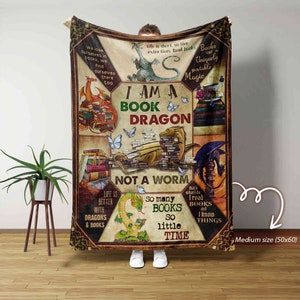 Puede incluir: Una manta de franela marrón y beige con un diseño de dragón de libro. La manta presenta un dragón hecho de libros, con el texto "Soy un dragón de libro, no un gusano". La manta también presenta otros diseños con temática de libros, como mariposas, libros y una taza de té.