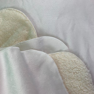 May include: Two layers of white fabric with a soft, fuzzy texture. The top layer is folded over to reveal the fuzzy underside.