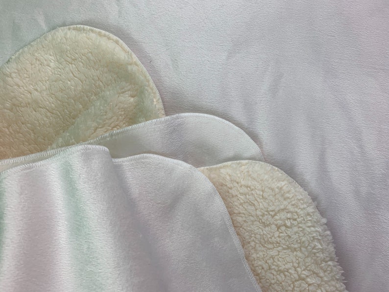 May include: Two layers of white fabric with a soft, fuzzy texture. The top layer is folded over to reveal the fuzzy underside.