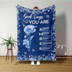 May include: A navy blue blanket with white floral and butterfly accents. The blanket features the text "God Says YOU ARE" and a blue poppy flower. The word "AMBER" is spelled out with additional words and Bible verses. Medium size: 50x60 inches.