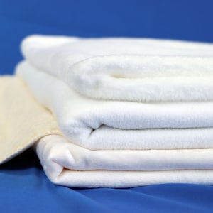 May include: A stack of four white towels, folded and arranged on a blue surface. The top towel is slightly off-center, creating a visually appealing composition.