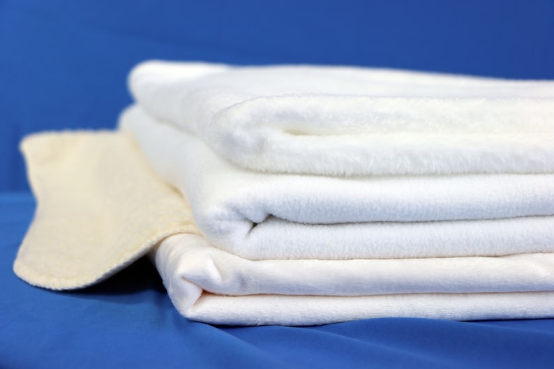 May include: A stack of four white towels, folded and arranged on a blue surface. The top towel is slightly off-center, creating a visually appealing composition.