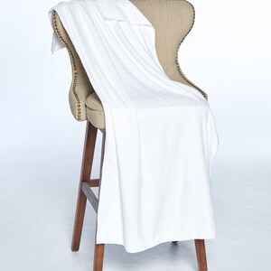 May include: A white throw blanket draped over a wooden chair with a beige fabric seat. The chair has a decorative nailhead trim.