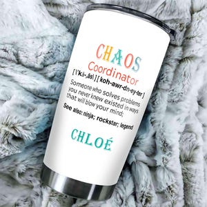 May include: A white stainless steel tumbler with the words "CHAOS Coordinator" in colorful text. The tumbler also includes a definition and the name "CHLO&Eacute;". The tumbler is on a soft, textured surface.