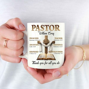 May include: White ceramic mug featuring the word "PASTOR" above the name "Wilson Cruz". The mug design includes a cross, an open book, and the text "Thank you for all you do".