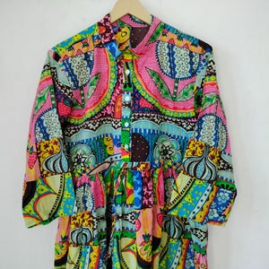 May include: A long-sleeved, colorful dress with a vibrant floral and geometric pattern. The dress features a button-down front, a ruffled skirt, and a collar. The dominant colors are pink, blue, green, and yellow.