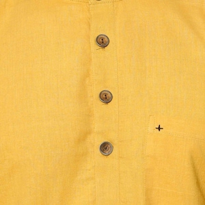 May include: A yellow linen shirt with a mandarin collar and wooden buttons. The shirt has a small pocket on the right side with a plus sign embroidered on it.