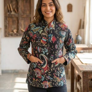 May include: A black quilted jacket featuring a vibrant, multi-coloured floral and paisley print. The jacket has a high collar, long sleeves, and two front patch pockets. The fabric has a textured, grid-like pattern throughout the entire garment.