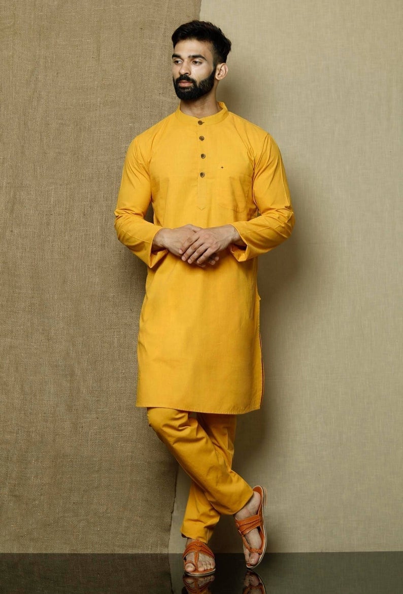 May include: A mustard yellow long-sleeved kurta with a button-up collar and side slits. The kurta is paired with matching pants and brown sandals.