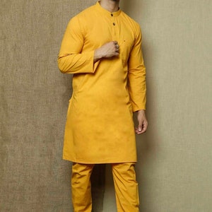 May include: A mustard yellow long-sleeved kurta with a mandarin collar and a button closure. The kurta is paired with matching mustard yellow pants. The model is wearing brown leather sandals.