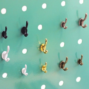 May include: A variety of small hooks in different colors and finishes, including gold, silver, and black, are displayed on a teal pegboard. The hooks are all about 1 inch in length and have a simple design.