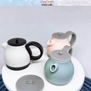 May include: Miniature electric kettles in white, pink, and teal with gray accents. One kettle has a detached lid. The kettles have black and gray handles. The image includes the text "STONE TOWER MINIATURE".