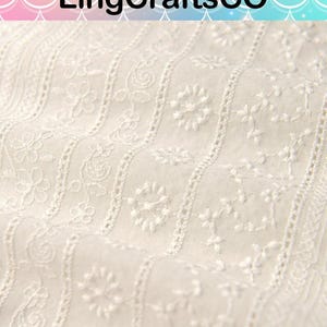 May include: Off-white fabric featuring vertical stripes of intricate white floral embroidery and delicate eyelet detailing. The textile displays a repeating pattern of small blossoms and vines, creating a textured surface with a consistent, repeating design.