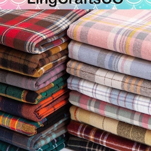 May include: Two stacks of folded fabric featuring various plaid and tartan patterns. The left stack includes red, brown, green, and dark blue tones. The right stack features lighter pastel shades of pink, blue, grey, and beige with white accents.