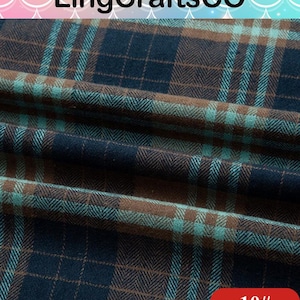 May include: A folded piece of fabric featuring a dark navy blue, brown, and teal plaid pattern with a visible herringbone weave texture. The textile displays a repeating grid design with intersecting lines of varying colors across the surface.