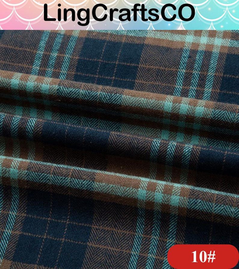 May include: A folded piece of fabric featuring a dark navy blue, brown, and teal plaid pattern with a visible herringbone weave texture. The textile displays a repeating grid design with intersecting lines of varying colors across the surface.