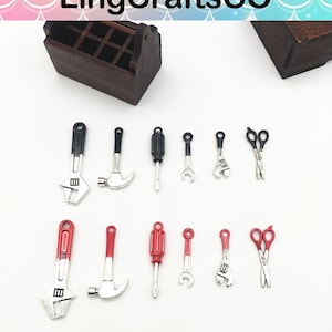 May include: Miniature silver and black tools, including wrenches, hammers, screwdrivers, and scissors, are arranged on a white surface. A wooden toolbox is visible in the background. The tools have red and black accents.