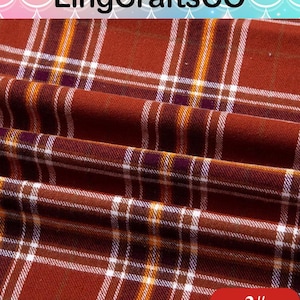 May include: A fabric with a rust-colored plaid pattern featuring thin white, yellow, and dark purple intersecting lines. The textile is folded, creating soft ripples across the surface. The text LingCraftsCO and 3# are visible.