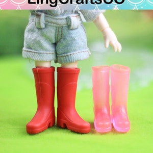 Könnte beinhalten: Ein Paar rote Gummistiefel und ein Paar rosa Gummistiefel. Die Stiefel sind für eine Puppe gemacht.