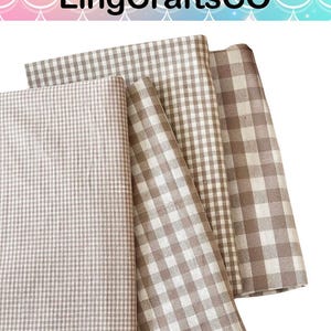 May include: Four folded pieces of fabric featuring various brown and white gingham check patterns. The textiles display different scales of checkered designs, ranging from small micro-checks to larger squares, all in neutral earth tones.