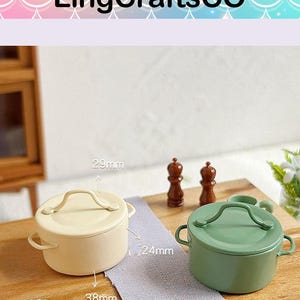 Può includere: Piccoli vasi in miniatura color crema e verde con coperchi, che misurano circa 3,8 cm di diametro e 2,9 cm di altezza. I vasi hanno manici e sono esposti su una superficie di legno. Sono visibili anche due piccoli macinapepe marroni.