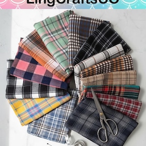 May include: A collection of folded fabric squares in various plaid patterns and colors, including pink, yellow, blue, green, brown, black, and white. A pair of silver metal scissors and a coiled white measuring tape are placed on the fabric.