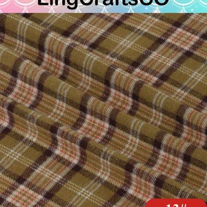 May include: Fabric featuring a plaid pattern in olive green, dark brown, white, and thin orange lines. The textile has a soft, slightly fuzzy texture with visible folds. The text LingCraftsCO appears at the top and 13# is in the bottom corner.