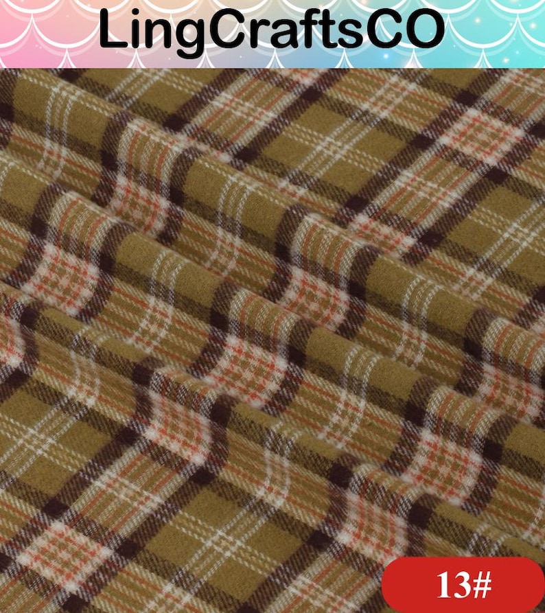 May include: Fabric featuring a plaid pattern in olive green, dark brown, white, and thin orange lines. The textile has a soft, slightly fuzzy texture with visible folds. The text LingCraftsCO appears at the top and 13# is in the bottom corner.