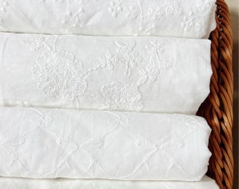 May include: Three rolls of white fabric featuring intricate white floral and bow embroidery patterns, stacked horizontally within a brown woven wicker basket. The text LingCraftsCO is visible at the top of the image against a colorful background.